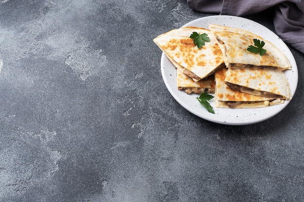 Quesadilla-Stücke mit Champignons, saurer Sahne und Käse auf einem Teller mit Petersilienblättern.