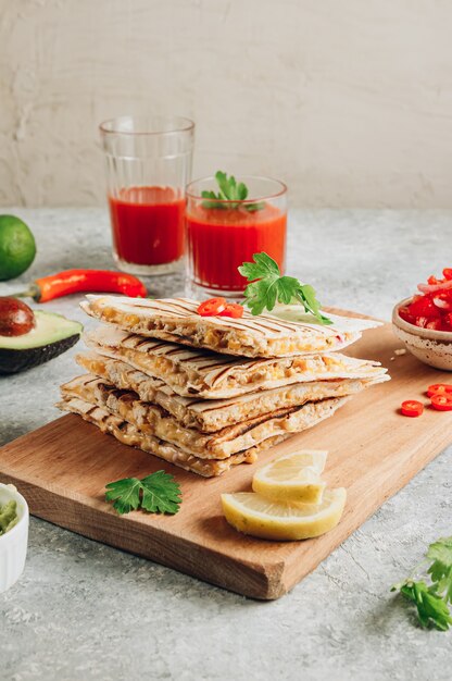 Quesadillas a la plancha sobre plancha de madera y con salsa y guacamole sobre fondo de piedra. Concepto de cocina mexicana Envoltura de quesadilla con pollo y maíz. Enfoque selectivo