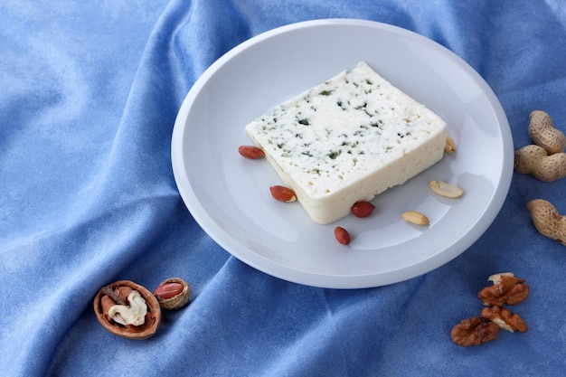 Queso aromático con moho azul y nueces en un plato blanco sobre un fondo azul Primer plano de una rebanada de queso dorblu