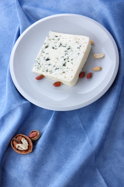 Queso aromático con moho azul y nueces en un plato blanco sobre un fondo azul Primer plano de una rebanada de queso dorblu