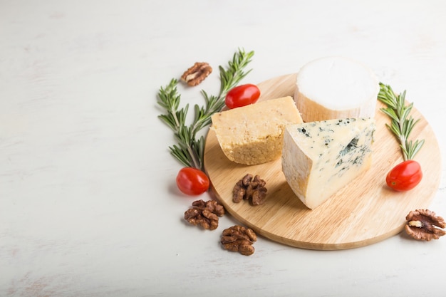 Queso azul y diversos tipos de queso con romero y tomates sobre tabla de madera sobre una superficie de madera blanca