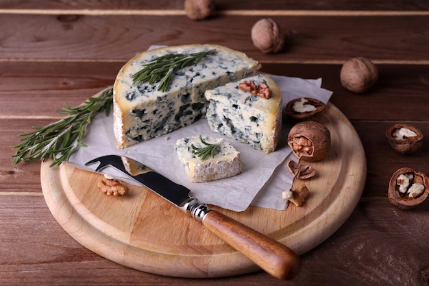 Queso azul con ramitas de romero y nueces a bordo con cuchillo y fondo de mesa de madera