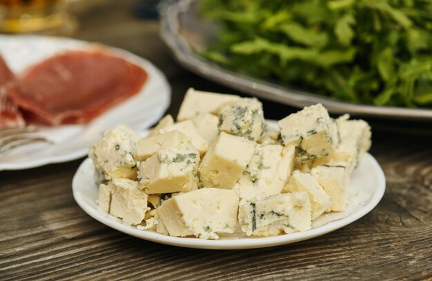 Queso azul sobre fondo de madera. Prosciutto y rúcula en el fondo