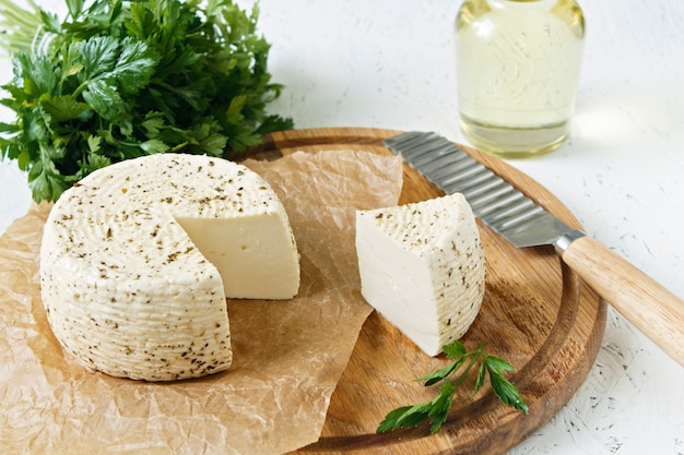 Queso blanco en una tabla de madera sobre un fondo blanco con verdes