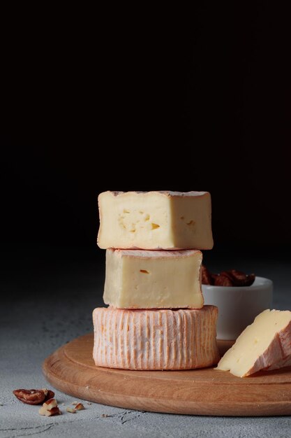 Queso blando en rodajas con moho en una tabla de madera sobre un fondo oscuro