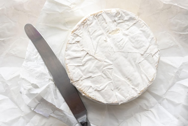 Queso brie y cubiertos de cocina en la vista superior de papel artesanal blanco