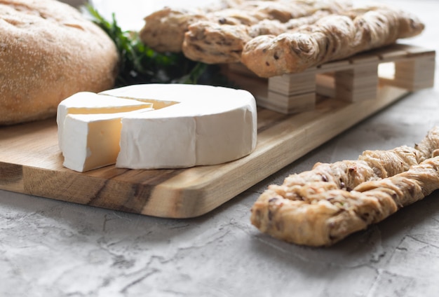 Foto queso brie con pan fresco y perejil sobre tabla de madera