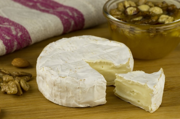 Foto queso brie y una rodaja sobre una tabla de madera con nueces