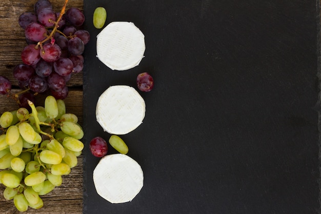 Queso brie en la tabla de cortar negra con uvas rojas y blancas, espacio de copia