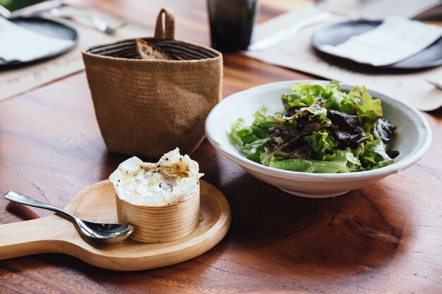 Queso Brie en el tablero de madera servido con ensalada de roble verde y pan recién horneado en rodajas.