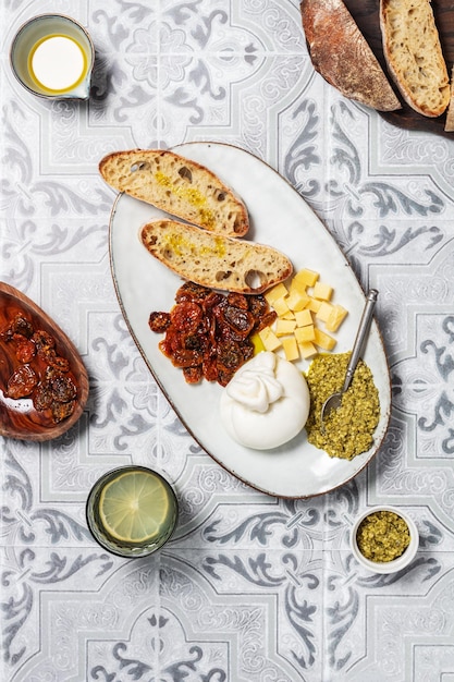 Foto queso burrata en un plato con pan, salsa pesto y tomates secos