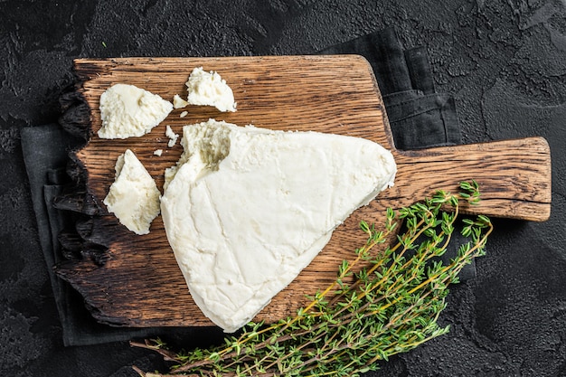 Queso de cabra suave fresco en una tabla de cortar con tomillo Fondo negro Vista superior