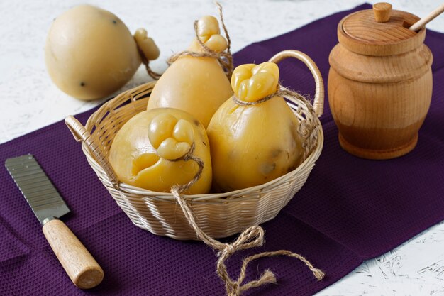 Foto queso caciocavallo con la miel en una cesta en un fondo blanco. pera de queso