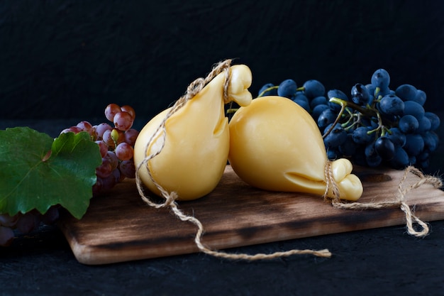 Queso Caciocavallo en un tablero de madera con las uvas en un fondo negro. Pera de queso