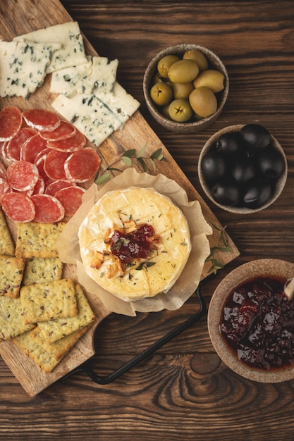 Queso camembert al horno con mermelada y aperitivos, sobre una tabla de madera, vista superior