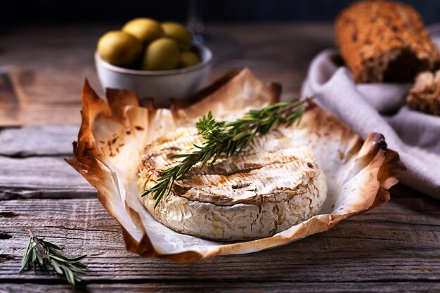 Queso camembert al horno con romero, aceitunas y pan, enfoque selectivo