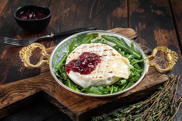 Queso Camembert Brie al horno con salsa de arándanos y adornado con ensalada de rúcula en una sartén Fondo de madera Vista superior