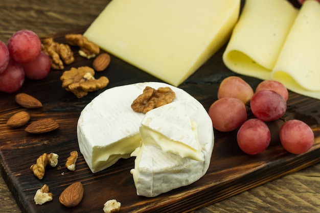 Queso camembert de corteza blanca y estructura suave y cremosa sobre tabla de madera con nueces y uvas.