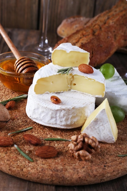 Queso camembert sobre papel, uvas, nueces y miel en un recipiente de vidrio sobre una tabla de cortar sobre fondo de madera