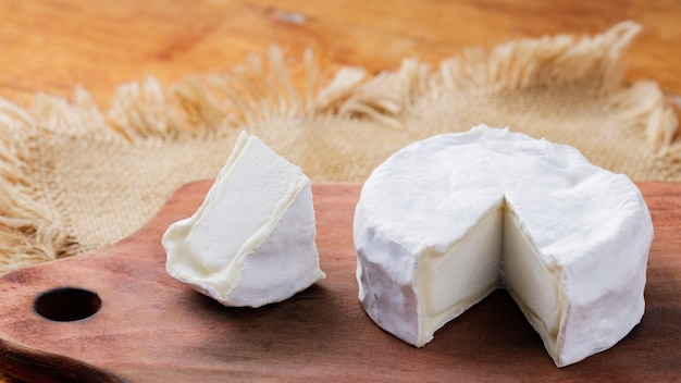 Foto queso camembert sobre una tabla de cortar de madera. queso blanco sobre un fondo de madera. copia espacio