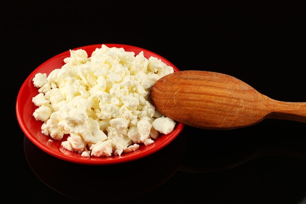 Queso casero en un plato y una cuchara sobre una superficie negra