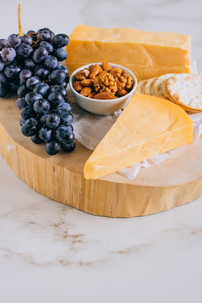 Queso cheddar, uvas, nueces, miel y galleta en tabla de madera sobre mármol