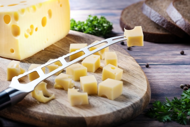 queso cortado en cubitos sobre una tabla de madera con un cuchillo