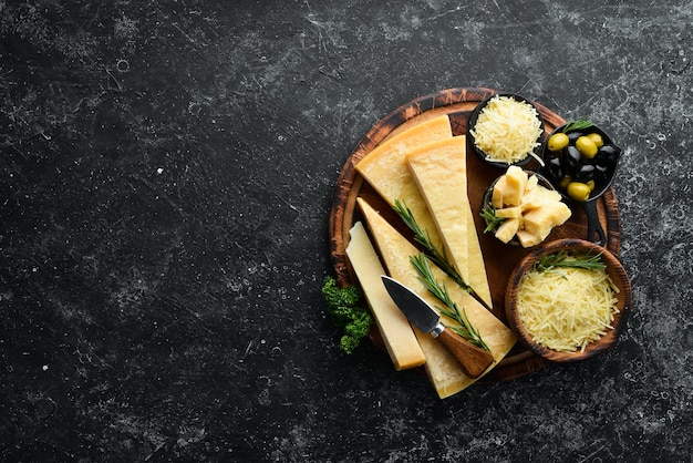 Queso duro con aceitunas y cuchillo de queso sobre fondo de piedra negra Parmesano Vista superior Espacio libre para el texto