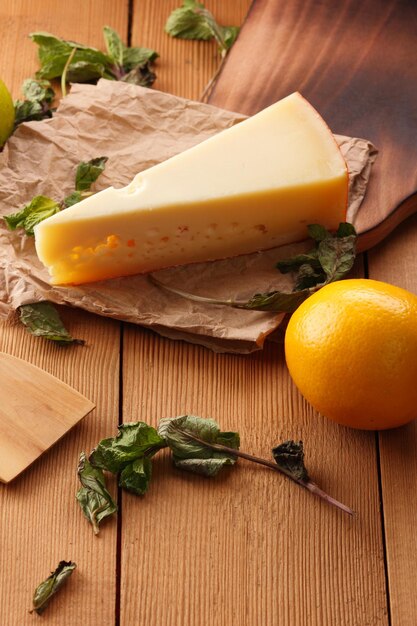 Queso duro amarillo sobre papel pergamino Un trozo de queso con cítricos menta seca sobre un fondo de madera Primer plano