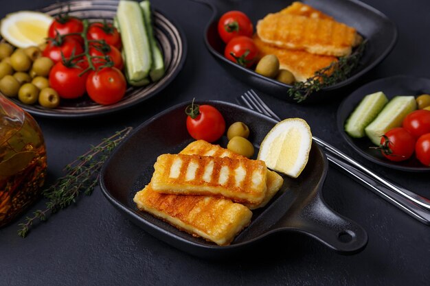 Queso halloumi a la parrilla en una sartén negra con aceitunas tomates pepinos tomillo y limón Queso tradicional del Mediterráneo oriental Fondo negro enfoque selectivo de primer plano