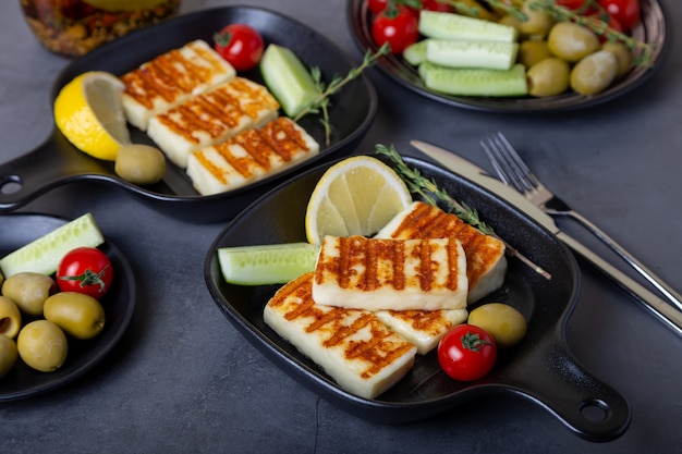 Queso haloumi a la parrilla en una sartén negra con aceitunas, tomates, pepinos y pepperoni. De cerca.