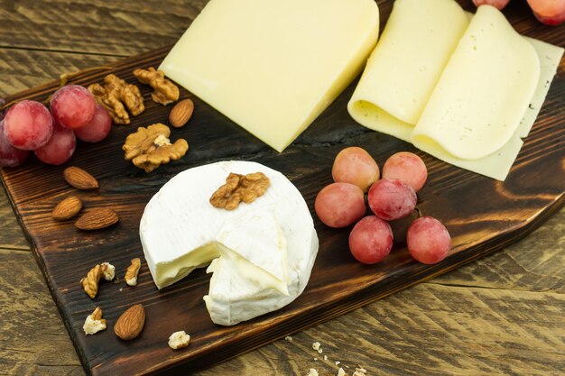 Queso Kamaber, parmesano, lonchas de queso crema sobre una tabla de madera y una mesa rústica con nueces y un pincel de uvas. vista superior.