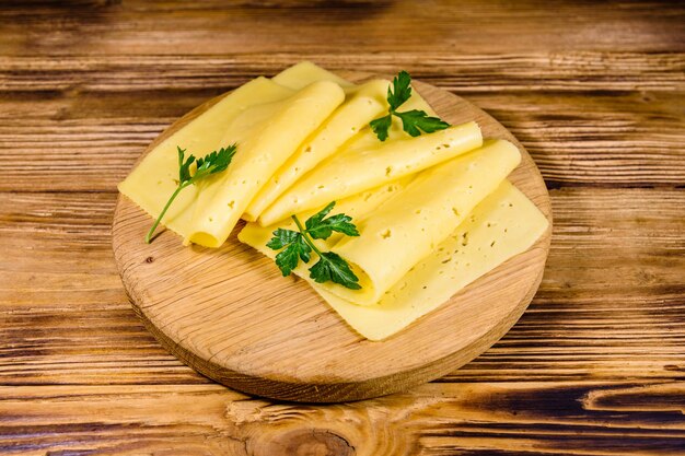 Queso en lonchas y perejil en una tabla para cortar madera