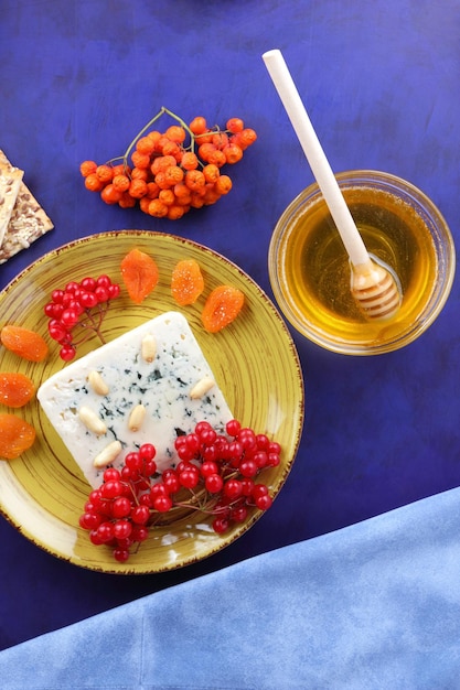 Queso con miel y una servilleta azul sobre un fondo azul Queso azul con nueces, bayas y frutos secos en un plato amarillo Vista de primer plano desde arriba