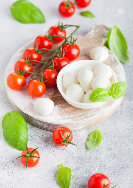 Queso Mini Mozzarella fresco en la tajadera vintage con tomates y hojas de albahaca sobre fondo de cocina de piedra.