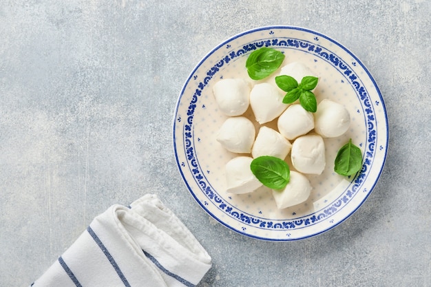 Queso mozzarella con albahaca en placa de cerámica blanca sobre fondo de piedra pizarra