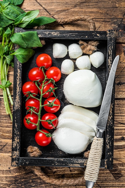 Queso mozzarella, albahaca y tomate cherry en bandeja de madera, ensalada Caprese. fondo de madera. Vista superior.