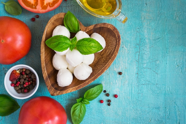 Queso mozzarella, tomate y albahaca sobre una mesa turquesa. Vista superior con espacio de copia.