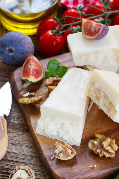 Queso parmesano sobre tabla de cortar de madera con tomates cherry, nueces e higos