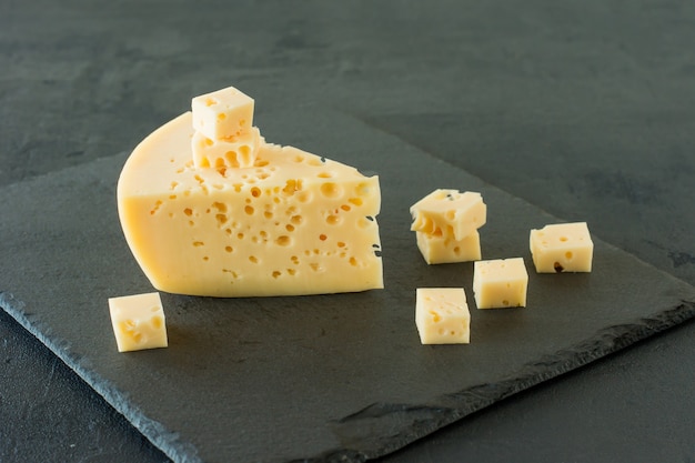 Queso Radamer sobre un fondo de hormigón negro. Trozo triangular de queso suizo de leche de vaca amarillo con agujeros.