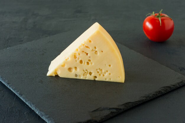 Queso Radamer sobre un fondo de hormigón negro. Trozo triangular de queso suizo de leche de vaca amarillo con agujeros.