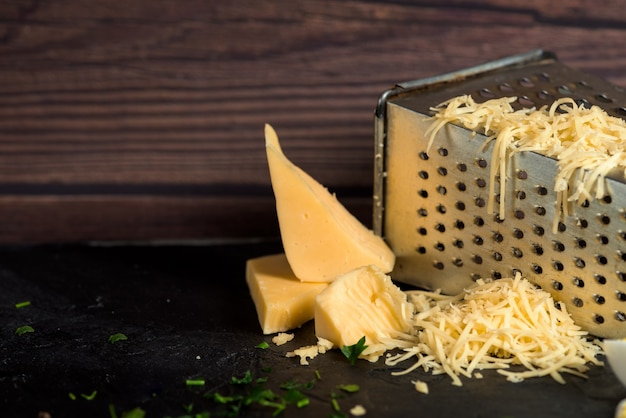 Queso rallado en un rallador sobre una mesa de madera oscura