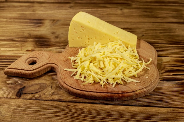 Queso rallado en tabla de cortar en mesa de madera