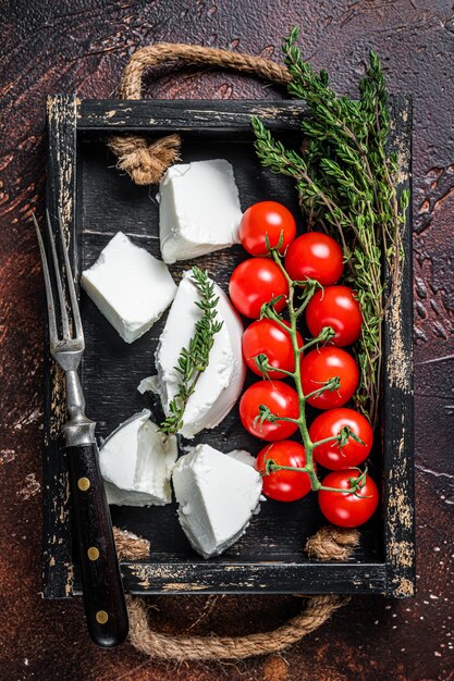 Queso ricotta crema en bandeja de madera con albahaca y tomate. Fondo oscuro. Vista superior.