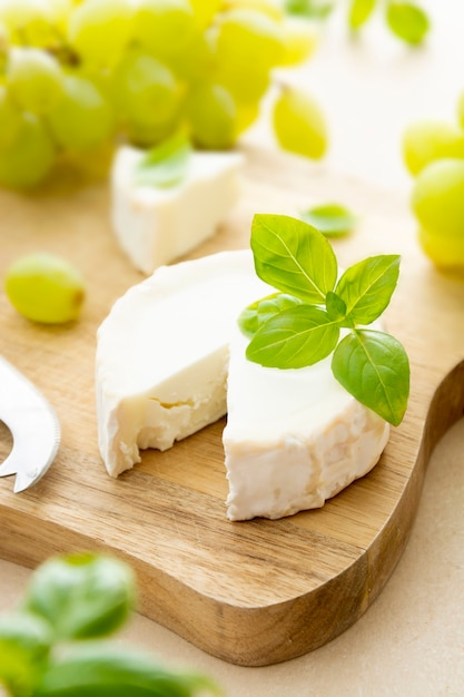 Queso de rueda blanca con hojas de albahaca. Queso de cabra sobre tabla de madera con albahaca y uvas