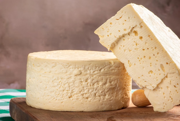 Queso semicurado de Brasil dispuesto en una tabla rústica sobre un mantel a cuadros verde y blanco, enfoque selectivo.