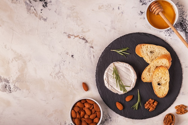 Queso servido en un plato con baguette, nueces surtidas y miel