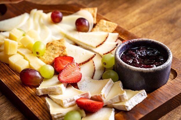 Queso surtido con frutas y mermelada sobre una tabla de madera. sirviendo la mesa y bocadillos al vino para el banquete.