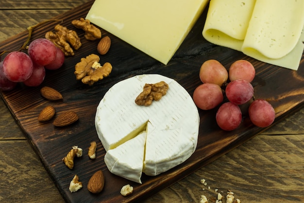 Queso tierno con moho blanco, queso francés, nueces y uvas rosadas sobre una tabla de madera. vista superior.