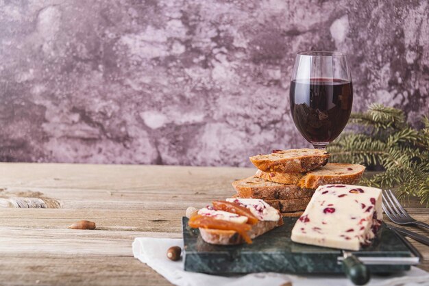 Queso Wensleydale con arándanos, vino tinto, miel, nueces, pasas sobre tabla de cortar de madera, fondo de hormigón negro, enfoque selectivo